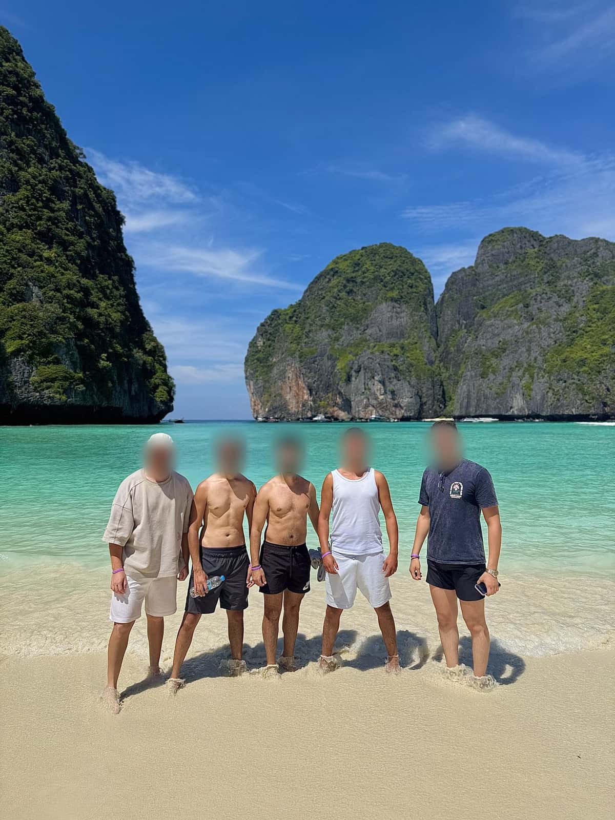 Five friends on a tropical beach in daylight, several of them shirtless