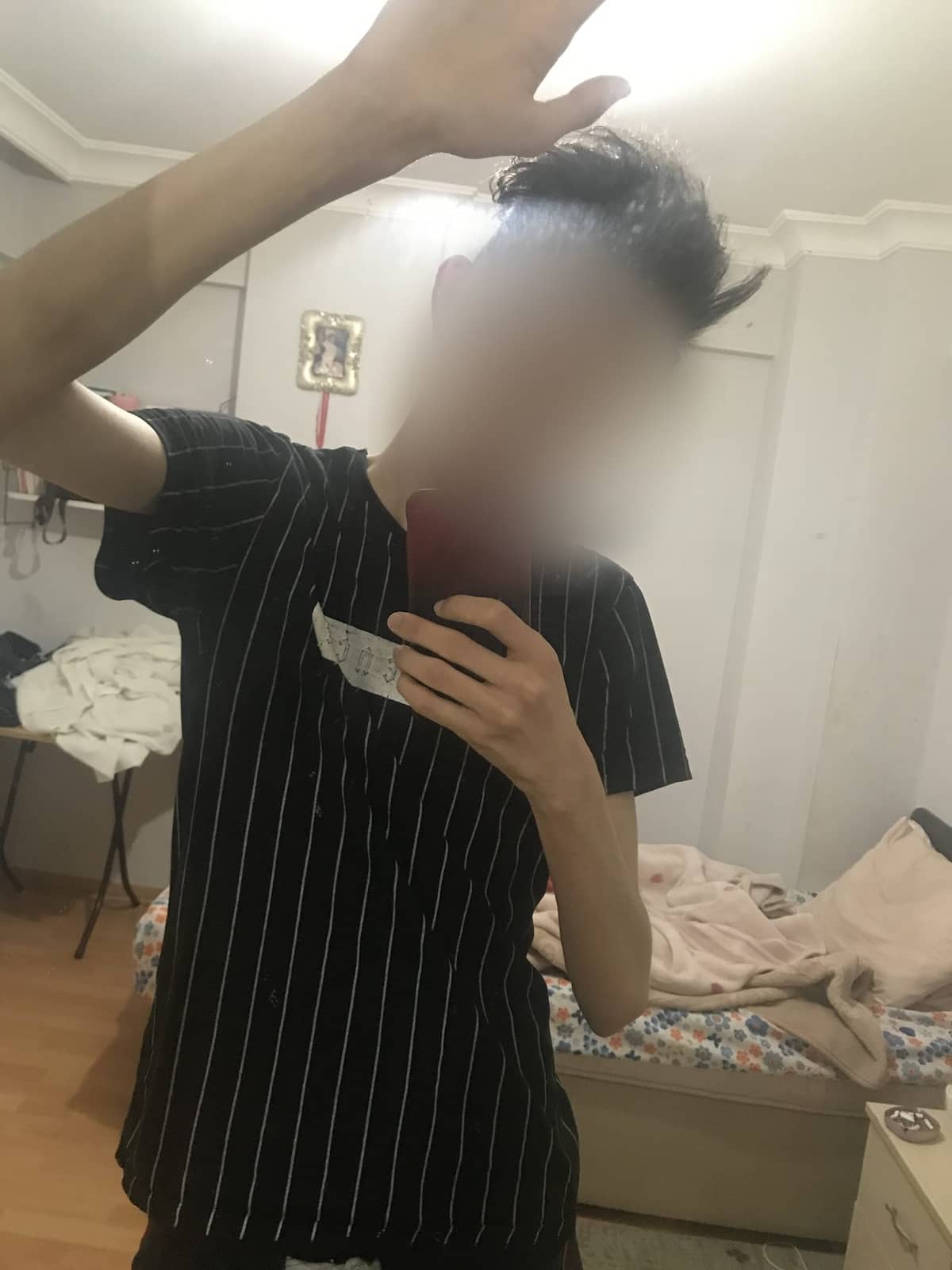 Mehdi in a loose striped t-shirt in his bedroom mirror, the shirt hanging off a thin frame