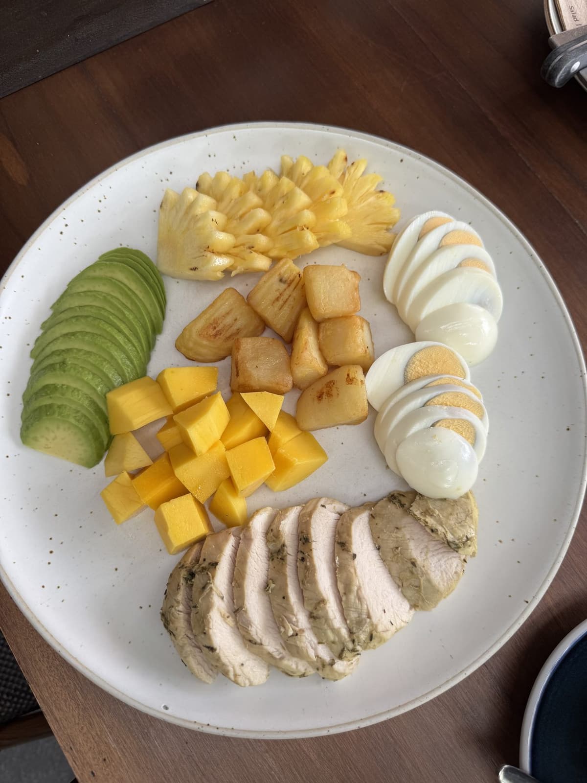 A dense plate from above: chicken, eggs, avocado, mango, potatoes and pineapple