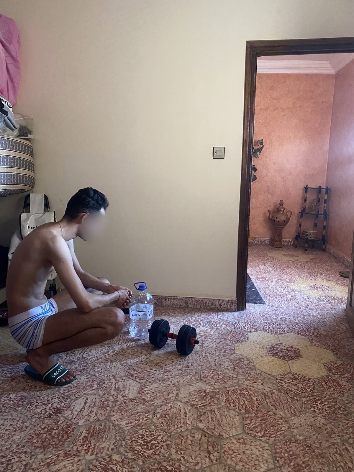 Mehdi at the start, crouching on his bedroom floor next to a pair of small dumbbells and a water bottle